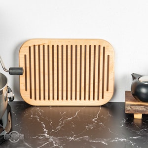 May include: A light wood bread board with a rectangular shape and a grooved surface. The board is sitting on a black marble countertop.