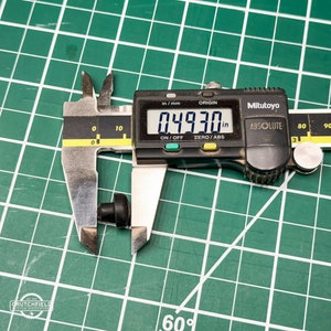 May include: A black digital caliper measuring a small black object. The caliper reads 0.4930 inches.