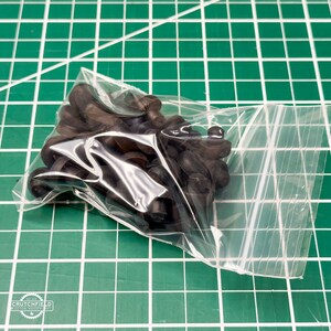 May include: A clear plastic bag filled with black rubber grommets. The grommets are in a pile and are all the same size.