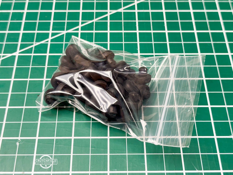 May include: A clear plastic bag filled with black rubber grommets. The grommets are in a pile and are all the same size.
