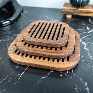 May include: Three wooden trivets stacked on top of each other. The trivets are made of dark brown wood and have a slatted design.