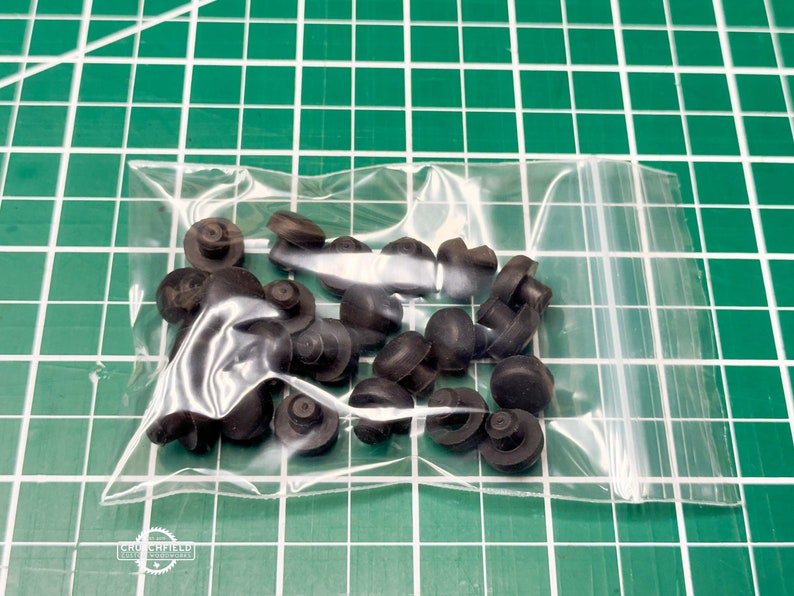 May include: A clear plastic bag containing black rubber bumpers. The bumpers are small and round with a raised centre.