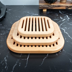 May include: Three wooden bread cooling racks stacked on top of each other. The racks are made of light brown wood and have a rectangular shape with a grooved design.