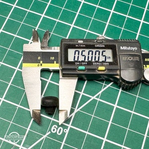 May include: A close-up of a digital caliper measuring a small black object. The caliper reads 0.5005 inches.