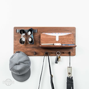 May include: A wooden wall organizer with hooks, a shelf, and a mail slot. It has a dark brown finish and is mounted on a white wall. There are sunglasses, a hat, keys, a purse, and an umbrella hanging on the organizer.