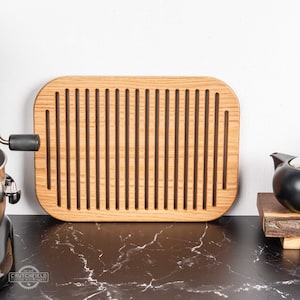 May include: A rectangular wooden bread board with a grooved surface. The board is made of light brown wood and has rounded edges.