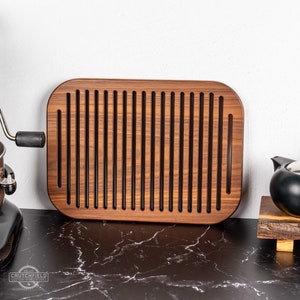 May include: A rectangular wooden bread board with a grooved surface for cooling bread. The board is made of dark wood and has rounded edges.