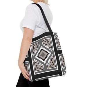 May include: A black tote bag featuring a geometric pattern in shades of gray, white, and beige. The design consists of a central diamond shape surrounded by nested rectangular frames with stepped, pixelated edges and solid black borders.