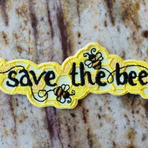 May include: Yellow embroidered patch with the text "save the bees" and two black and yellow bees. The patch is designed to look like a honeycomb.