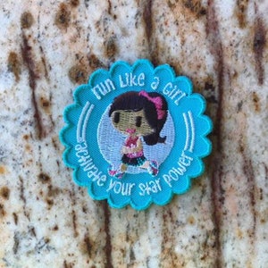 May include: A turquoise blue embroidered patch with a white scalloped border. The patch features a cartoon girl running with the text "Run like a girl - Activate your star power" in white.