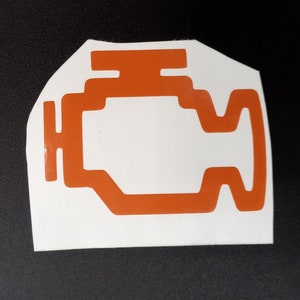 May include: Orange engine-shaped sticker on a white background. The sticker is a warning light symbol, commonly found on a car's dashboard. The sticker is on a black surface.