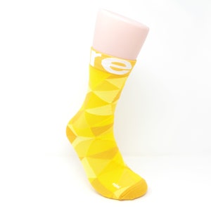 Könnte beinhalten: Gelbe Socken mit geometrischem Muster und dem Wort "rebel" auf der Unterseite. Die Socken befinden sich auf einem weißen Mannequin-Fuß.