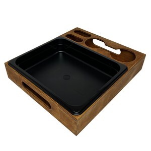 May include: A wooden tray with a black plastic insert. The tray has a cutout for a cup or mug and a small compartment for a utensil.
