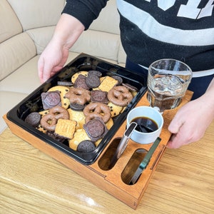 May include: A wooden serving tray with a black tray insert, a glass of water, a cup of coffee, and a variety of cookies and pretzels.