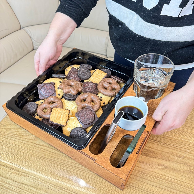 May include: A wooden serving tray with a black tray insert, a glass of water, a cup of coffee, and a variety of cookies and pretzels.