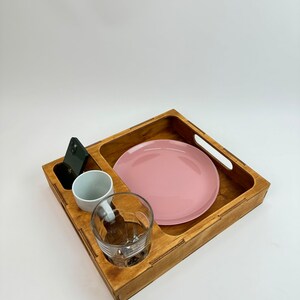 May include: A wooden tray with a pink plate, a white cup, a glass, and a black phone.