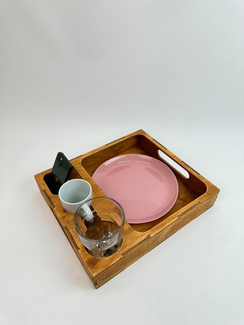 May include: A wooden tray with a pink plate, a white cup, a glass, and a black phone.