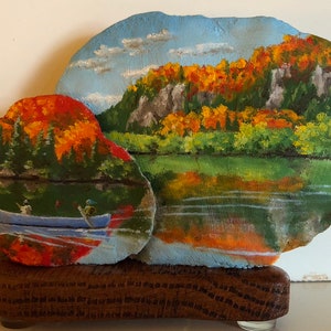 Pode incluir: Cena de paisagem pintada à mão em uma rocha, retratando um lago com uma canoa e figuras, e uma montanha com folhagem de outono. A obra de arte é montada em uma base de madeira, criando uma peça decorativa única.
