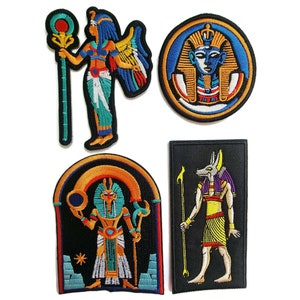 Könnte beinhalten: Satz von vier gestickten Bügelbildern mit ägyptischen Gottheiten. Die Patches sind farbenfroh und weisen komplizierte Details auf. Die Patches beinhalten eine Frau, die einen Stab hält, einen Pharaonenkopf, einen Schakalgott und einen Gott mit einer Sonnenscheibe.