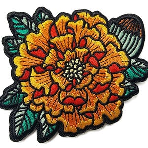 May include: Embroidered floral patch featuring a vibrant orange and yellow flower with red accents. The flower is surrounded by green leaves and outlined with black thread. This decorative patch can be applied to clothing or accessories.