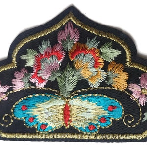 Op de afbeelding: Geborduurde patch met een zwarte achtergrond, met een vlinder en bloemenontwerp. De vlinder heeft turquoise vleugels met rode en gouden accenten. De bloemen zijn in tinten roze, rood en geel, met gouden afwerking.
