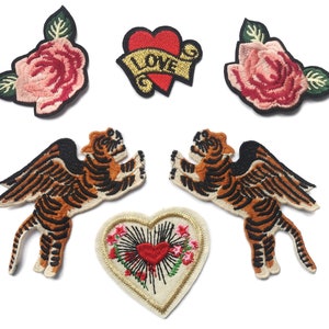 May include: A collection of embroidered patches featuring a heart with "LOVE" on a banner, two pink roses, two winged tiger figures, and a heart with floral and sunburst details. Each patch has a black border.