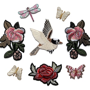 Puede incluir: Parches bordados con varios diseños inspirados en la naturaleza. Incluye un pájaro con las alas extendidas, mariposas, una libélula y varios parches florales con rosas rosas y rojas. Los parches están sobre un fondo blanco.