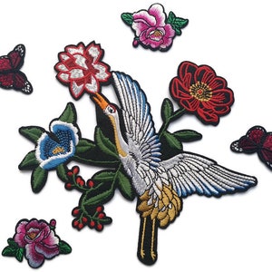 May include: Embroidered patches featuring floral and bird designs. The patches include a crane, flowers in red, pink, and blue, and butterflies. The patches have a black border and are designed for clothing or craft projects.