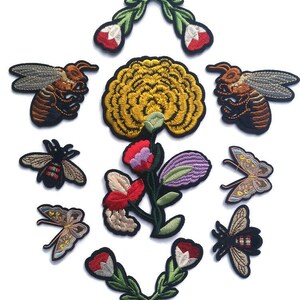 Puede incluir: Un conjunto de parches bordados con motivos florales e insectos. Los parches representan abejas, mariposas y flores en varios colores, incluyendo amarillo, rojo, morado y verde. Cada parche tiene un borde negro.