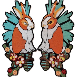 May include: Two embroidered patches featuring a rabbit design. The rabbits have orange and white bodies, with blue and green accents. They are perched on branches with colorful flowers. The patches are outlined in black.