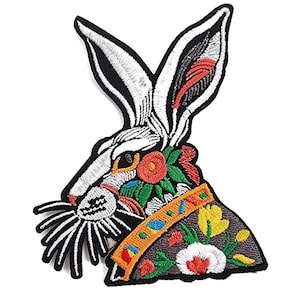 Könnte beinhalten: Gestickter Bügel-Patch mit einem weißen Kaninchen mit bunten floralen Details und einem schwarzen Umriss.