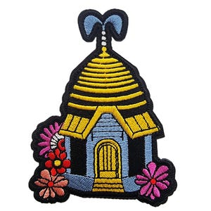 May include: Embroidered patch with a beehive design. The patch has a black outline, a yellow and black beehive, a blue house, and colourful flowers in pink, red, and orange. The patch is designed for decorative purposes.