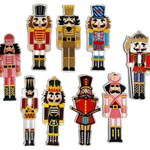May include: Ten embroidered nutcracker patches in various colours. Each patch features a detailed design of a nutcracker soldier with a hat, uniform, and facial features. The patches are in shades of red, blue, gold, and pink.