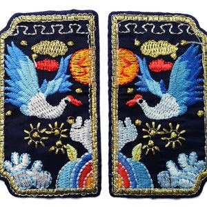 May include: Two embroidered patches with a navy blue background. Each patch features a crane with blue wings, a red sun, and gold accents. The patches are outlined with gold thread and have a decorative top edge.