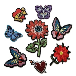 May include: A collection of embroidered patches featuring various designs. Included are butterflies, flowers, and a heart with the word "LOVE". The patches are in vibrant colors like red, blue, purple, and yellow, with detailed stitching.