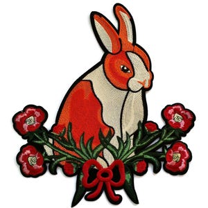 Puede incluir: Parche bordado para planchar con un conejo blanco y naranja sentado en un lecho de hojas verdes y flores rojas.
