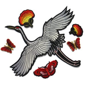 May include: An embroidered patch set featuring a large white crane with silver and black details in flight, surrounded by two red and yellow floral motifs and two red butterflies with gold accents, all with black borders on a white background.