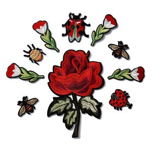May include: Embroidered patches featuring a large red rose, ladybugs, bees, and flowers. The patches have a black border and are designed with detailed stitching. The patches are ideal for decorating clothing, bags, or other fabric items.