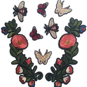 May include: A set of embroidered iron-on patches featuring floral designs, butterflies, and bees. The patches are in shades of red, pink, green, white, and black.