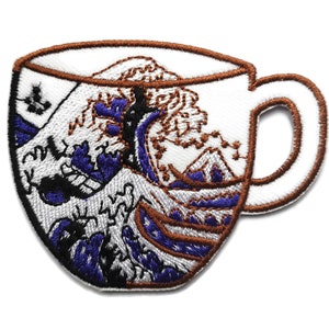 May include: White ceramic coffee mug featuring an embroidered design of The Great Wave off Kanagawa, a renowned Japanese woodblock print by Hokusai. The wave is depicted in shades of blue and brown, with white foam crests.