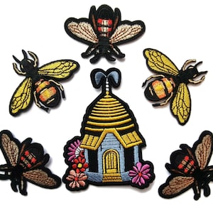 May include: A set of six embroidered iron-on patches featuring a beehive with flowers and five bees. The beehive is blue and yellow with a brown roof. The bees are black and yellow with brown wings. The flowers are pink, yellow, and orange.