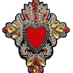 May include: Embroidered patch with a red heart centre, surrounded by gold and silver metallic thread, red and yellow gemstones, and black fabric. The patch has an ornate, decorative design.