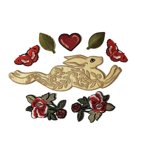 May include: A collection of embroidered patches featuring a central beige rabbit with intricate floral scrollwork, two red butterflies, two green leaves, a red heart, and two floral clusters with red and white blossoms and green leaves.