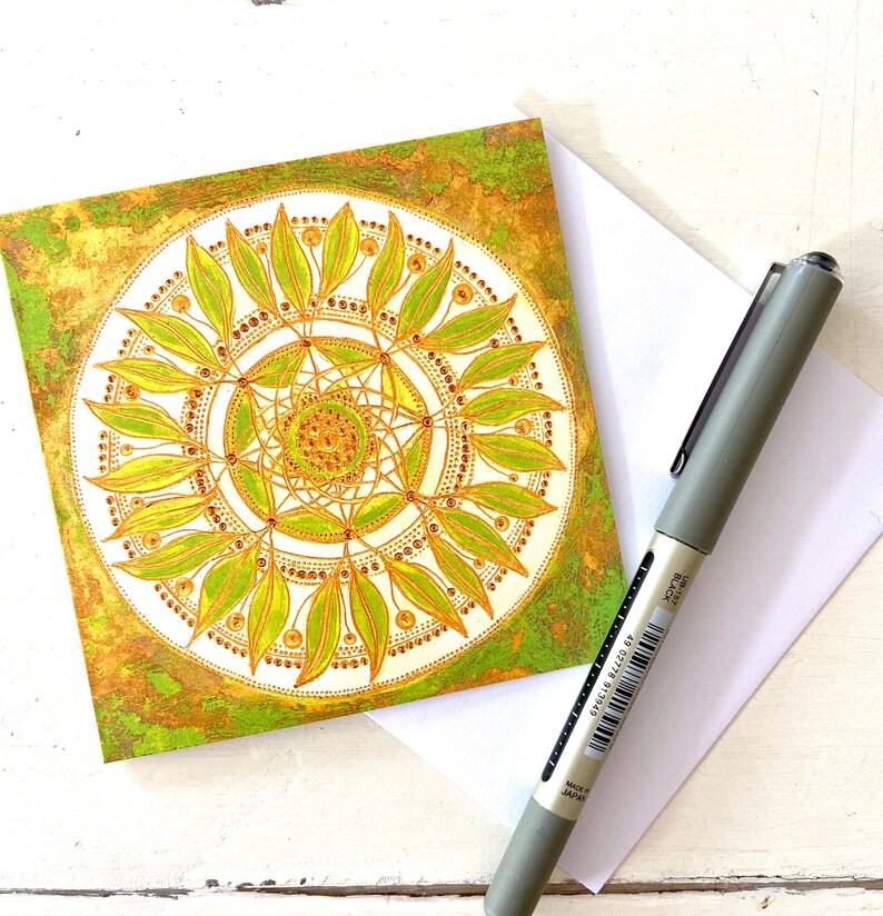 May include: A green and gold mandala card with a circular design featuring leaves and dots. The card has a textured background.