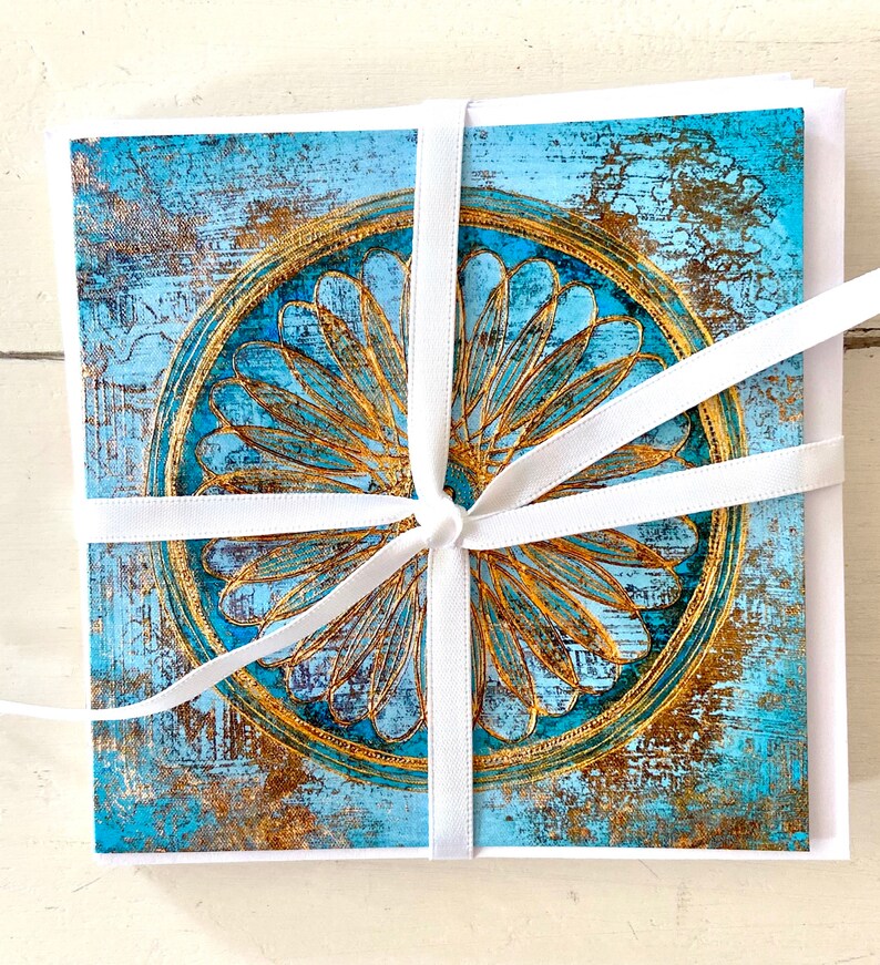May include: A set of greeting cards featuring a blue and gold mandala design. The cards are tied together with a white ribbon.