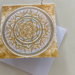 May include: A gold and blue mandala with pink floral accents on a textured gold background. The mandala is a circular design with intricate details and a geometric pattern.