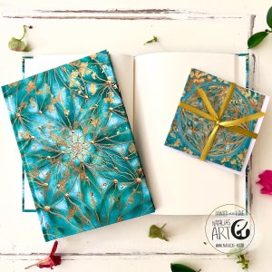 Könnte beinhalten: Ein türkisfarbenes und goldenes Journal mit einem Mandala-Design auf dem Cover. Das Journal ist geöffnet und zeigt eine leere Seite. Eine passende türkisfarbene und goldene Karte mit einem Mandala-Design ist ebenfalls enthalten. Die Karte ist mit einem goldenen Band gebunden.
