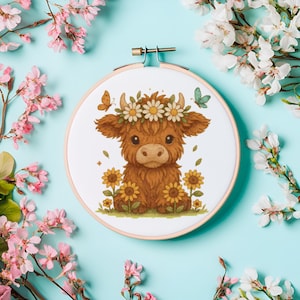May include: A circular embroidery hoop with a cartoon Highland cow illustration. The brown cow wears a daisy crown and is surrounded by sunflowers and butterflies. Set against a light blue backdrop, with pink and white flowers.