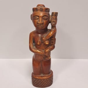 May include: A wooden sculpture of a woman holding a child. Both figures are wearing crowns. The sculpture is carved in a traditional style and has a dark brown color.