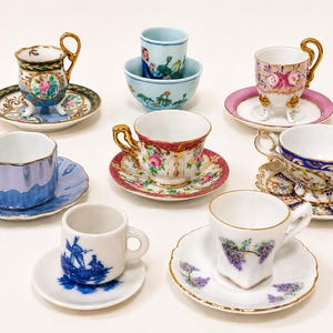 May include: A collection of eight miniature porcelain teacups and saucers, including various floral patterns, gold-trimmed edges, and a blue and white windmill design. The set features diverse shapes, including footed cups and a small bowl.
